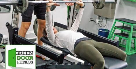 man on weight bench with trainer spotting him, Green Door logo in bottom left corner