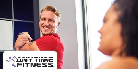 man with a red shirt and blonde hair stretching his arm and smiling, anytime fitness logo in bottom left corner
