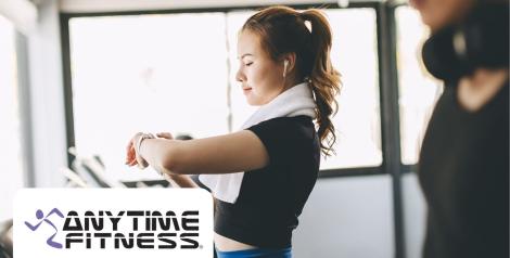 woman with black shirt and blue pants, checking her watch on the treadmill, anytime fitness logo on bottom left corner
