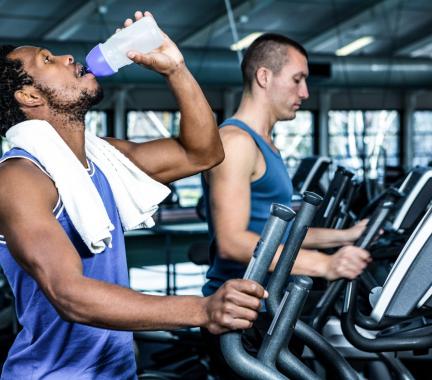 man with beard and dark hair drinking from a water bottle, on a treadmill