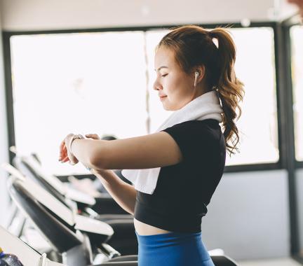 woman with black shirt and blue pants, checking her watch on the treadmill