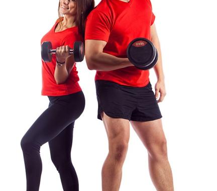 woman and man standing back to back with red shirts, black bottoms and holding a free weight