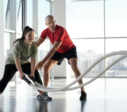 a woman using fitness ropes and a man in a red shirt appears to be coaching her on technique