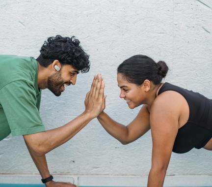man wearing a green shirt giving a high five to a woman with a black tank top on, both are doing a push up