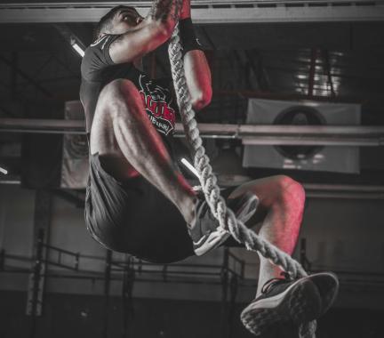 man climbing a rope in a dark gym