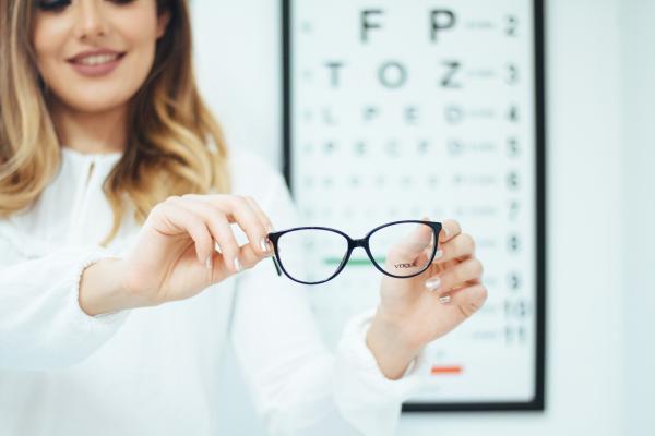 Woman holding a pair of glasses in front of an eye chart