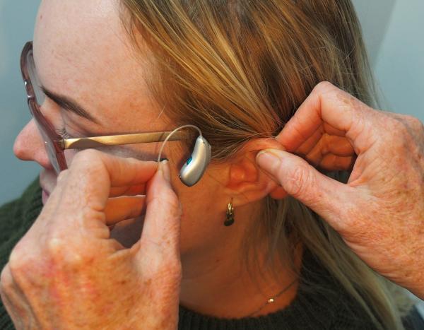 hands putting hearing aid on for woman