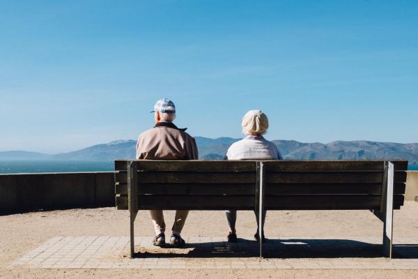 older man and woman sitting on a park bench looking at a mountain view